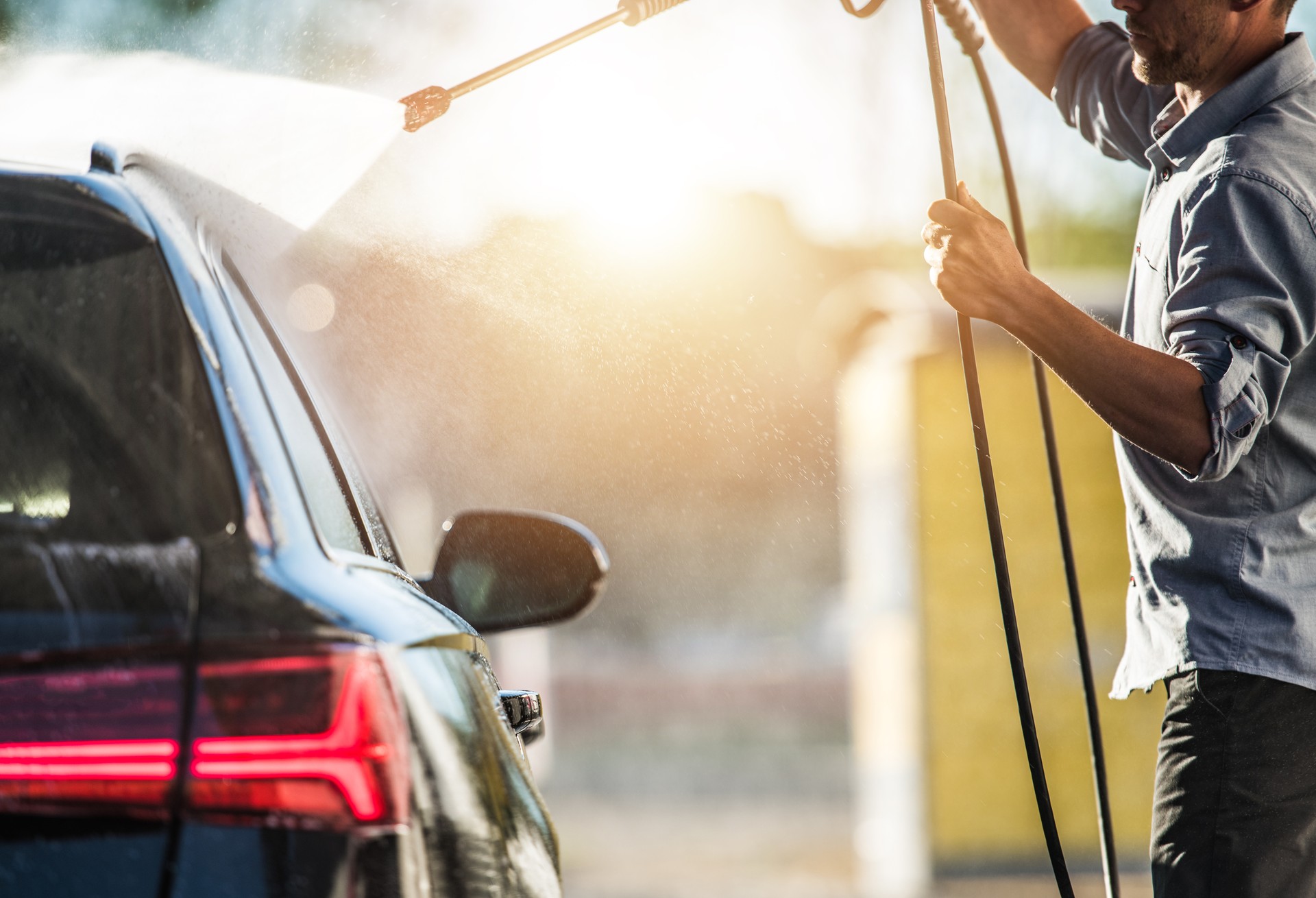 Caucasian Car Wash Worker Cleaning Exterior Of Customers Car By Spraying Water And Rinsing Dirt