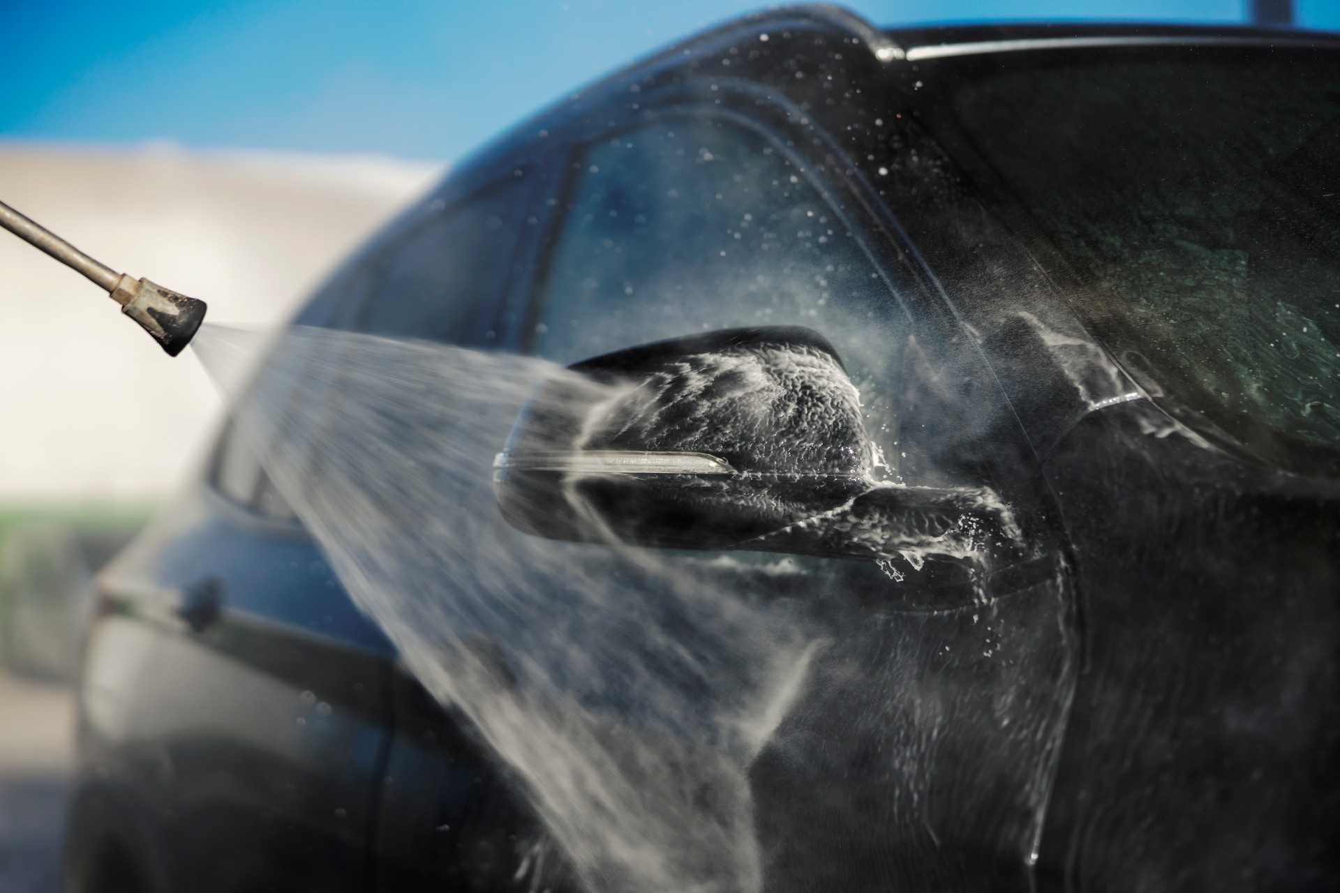 Close up of a water jet gun washing a rear view mirror.