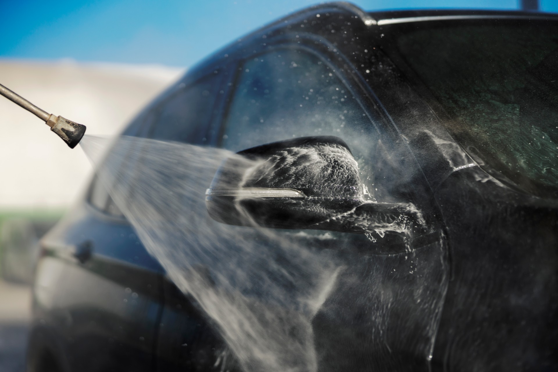 Close up of a water jet gun washing a rear view mirror.